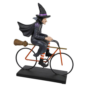 A classic witch riding bicycle with a black hat, orange striped socks, and a broom on the handlebars from witches conservatory