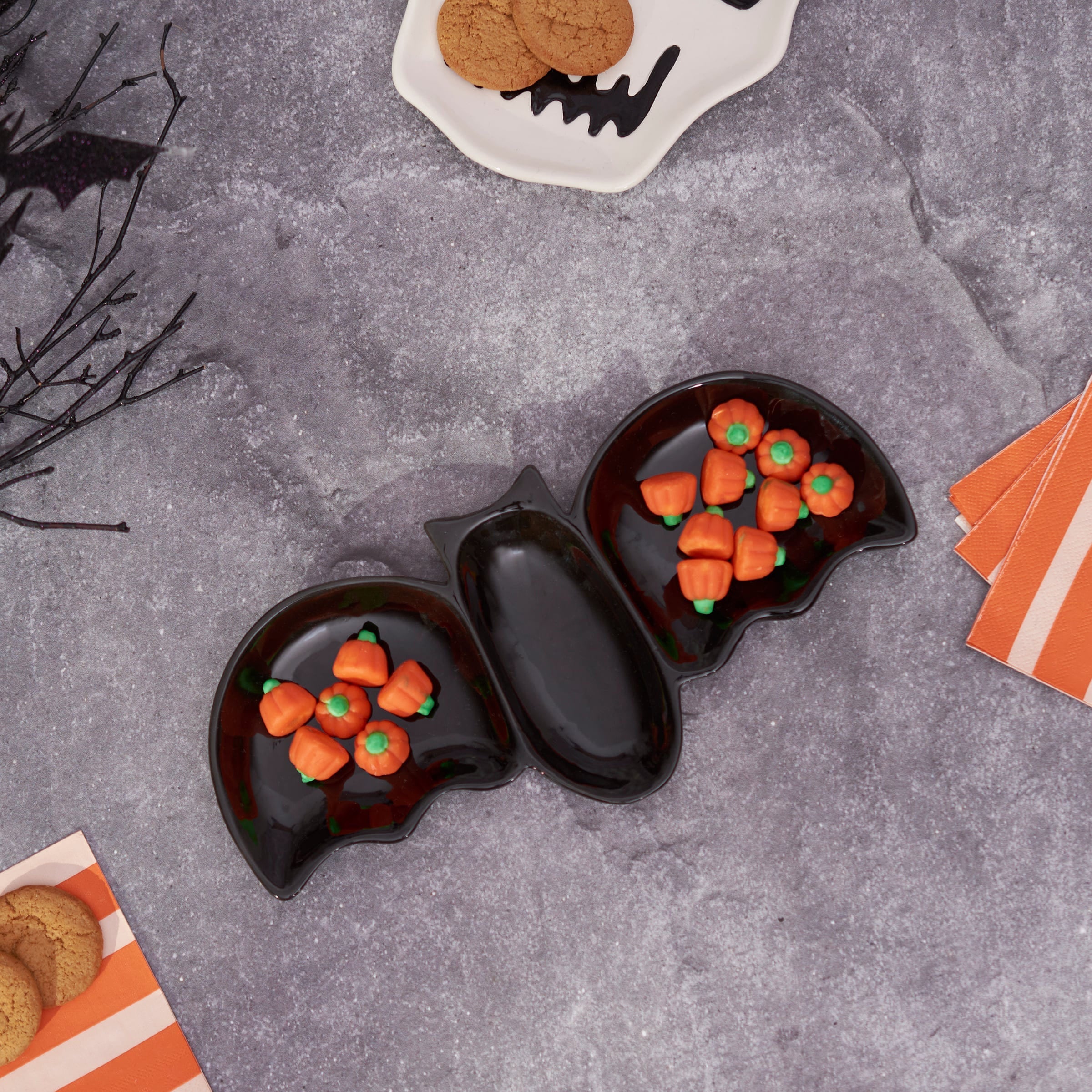 Black ceramic flying bat tray with two compartments holding orange pumpkin candies for snacks and treats