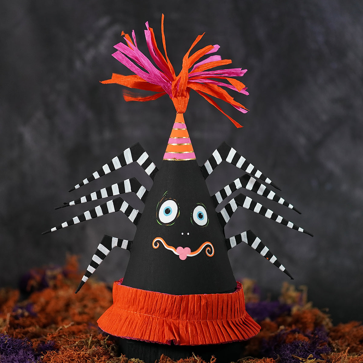 A whimsical black paper spooky spider party favor cone box with striped legs blue eyes and an orange ruffled base