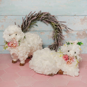 Two plush white lying sheep figurines with flower wreaths spreading holiday cheer on fluffy white bodies