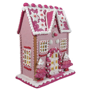 A 13 inch lighted pink gingerbread house ornament with glitter, white icing, candy decorations, and miniature trees