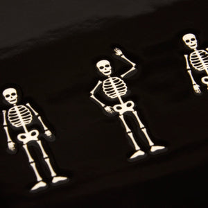 White skeleton-shaped enamel pins with black outlines in playful poses on a dark background for skeletons oval platter