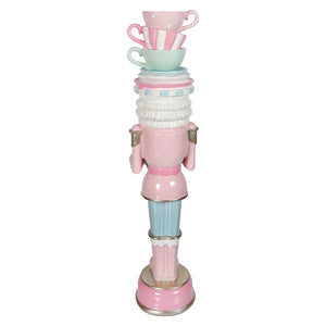 A whimsical pastel resin dessert toy soldier balancing teacups in pink with a stack of decorative cups on its head