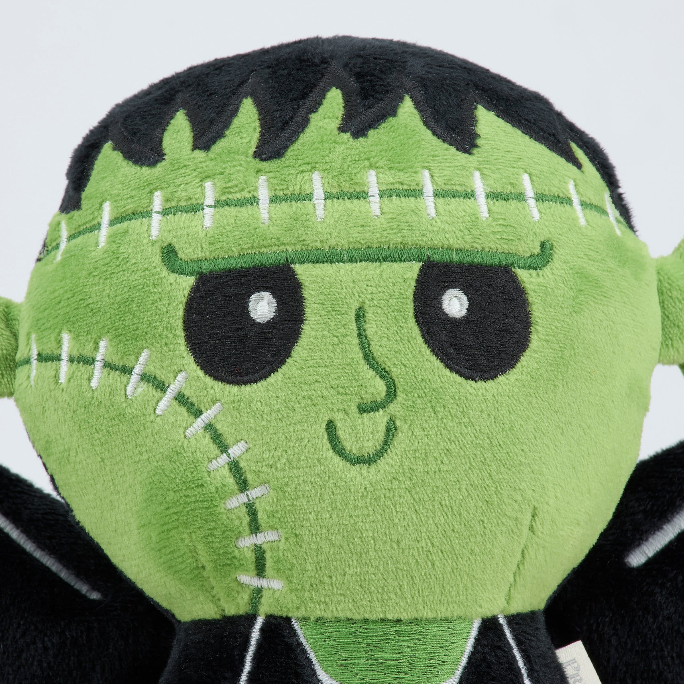 Green plush frankenbat shaped pillow with black stitched hair and embroidered facial features for cozy use
