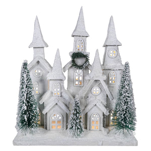 White snow-covered frosted wood house figurine with led lighted winter holiday glowing windows and bottle brush trees