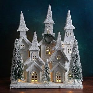 White frosted wood house with led lighted winter holiday windows and snow dusted bottle brush trees decor piece