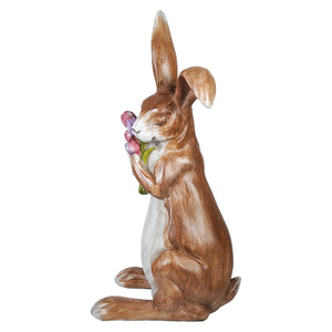 Serene brown bunny resin figurine sitting upright clutching spring floral bouquet with pink flowers
