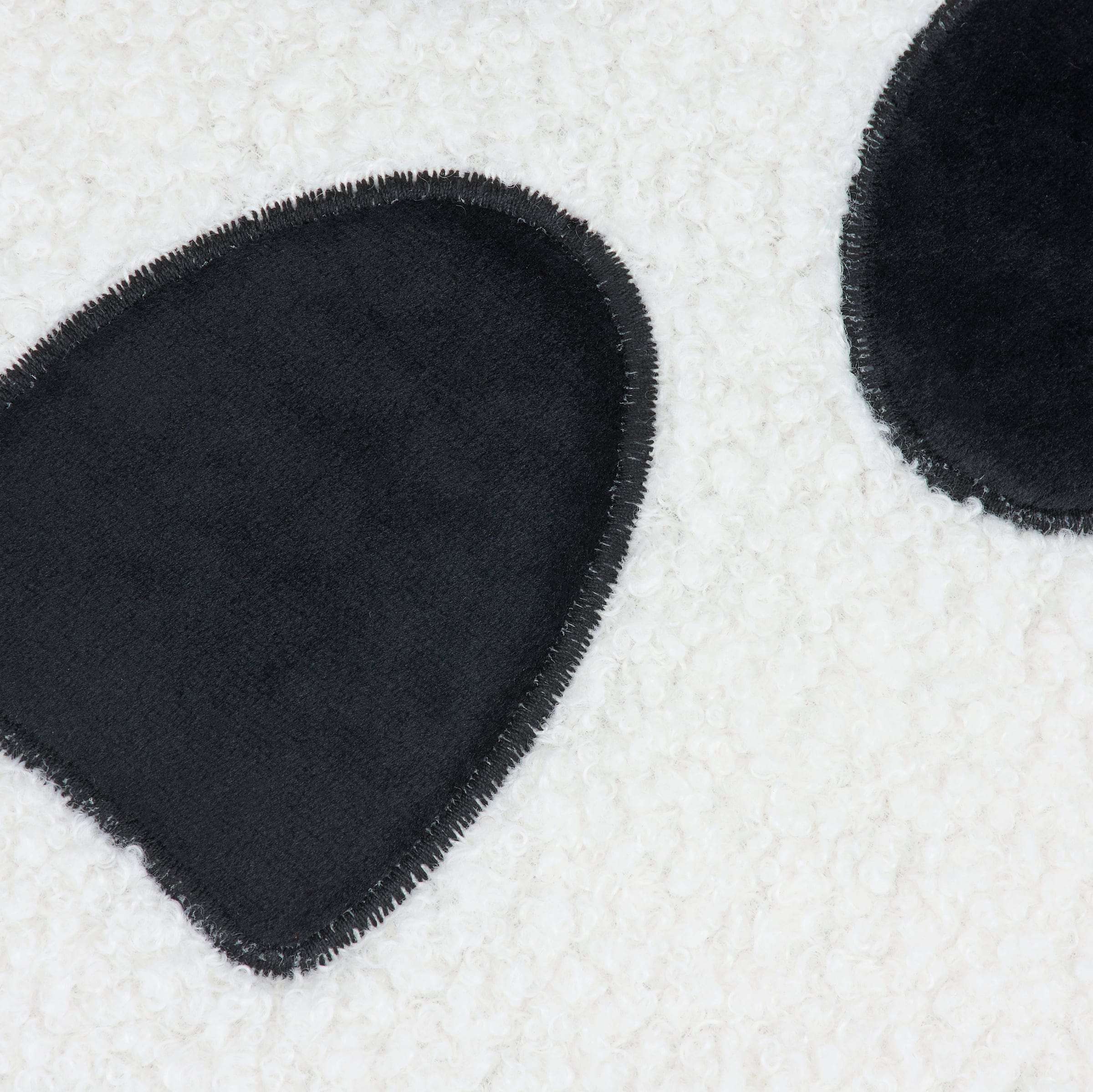 Black plush panda ear patch with fuzzy texture and frayed edge on ghost shaped pillow
