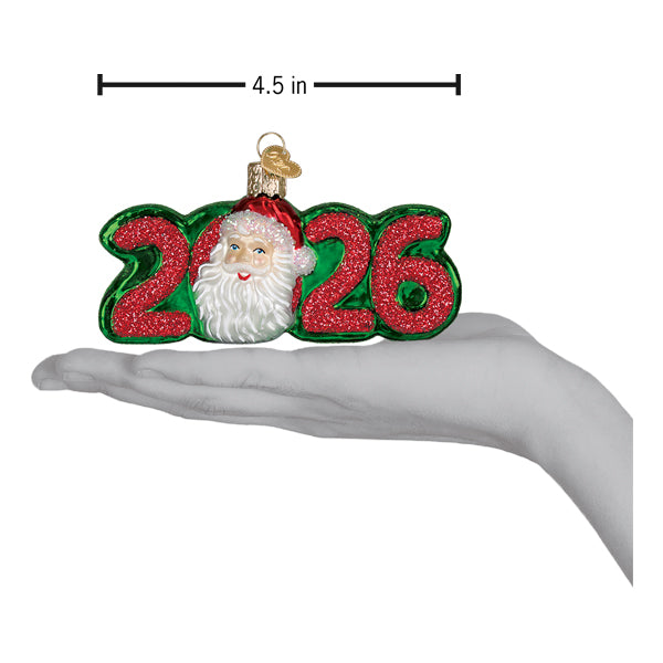 A christmas glass ornament featuring a glittery red 2026 and a smiling santa face on green with gold cap santa ornament