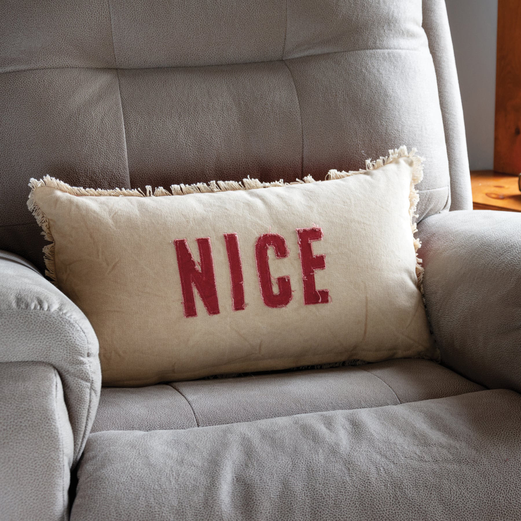 Cream-colored dan dipaolo holiday pillow with frayed edges and bold red nice lettering perfect for believe pillow fans