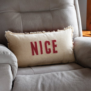 Cream-colored dan dipaolo holiday pillow with frayed edges and bold red nice lettering perfect for believe pillow fans