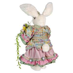 A plush white vintage easter bunny figurine in a floral pink and green ruffled dress holding a bouquet of flowers