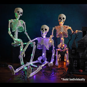 Three illuminated plastic skeletons glowing green purple and orange in halloween lights and decor setup