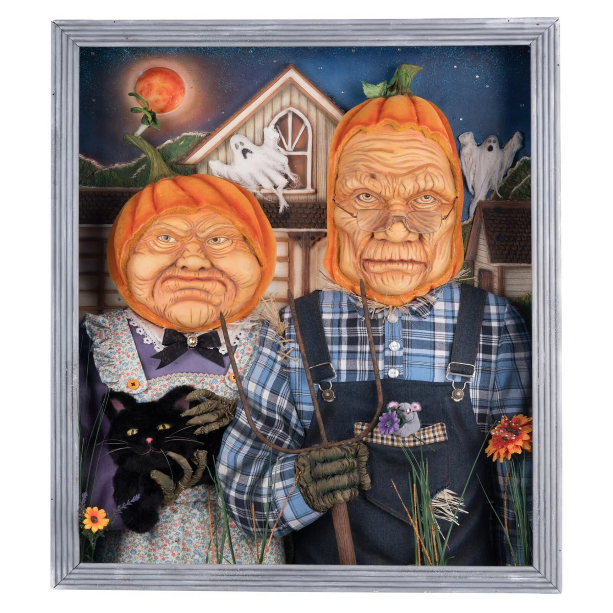A framed Halloween art print featuring two scarecrows with pumpkin heads, a black cat, ghosts, and a haunted house under a full moon, enclosed in a silver frame.