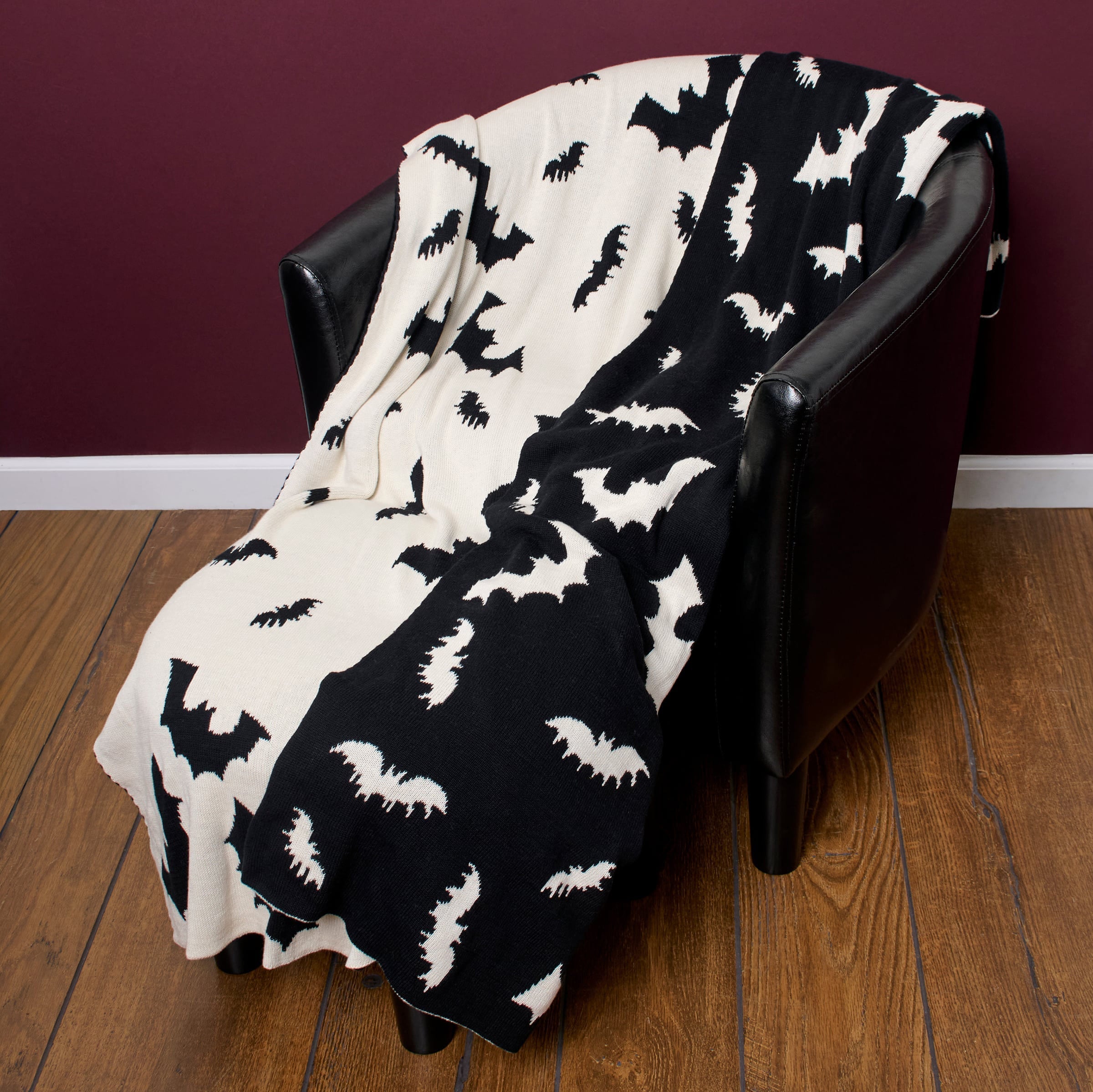 Black and white bat-patterned knit throw blanket draped over a black leather armchair for cozy decor