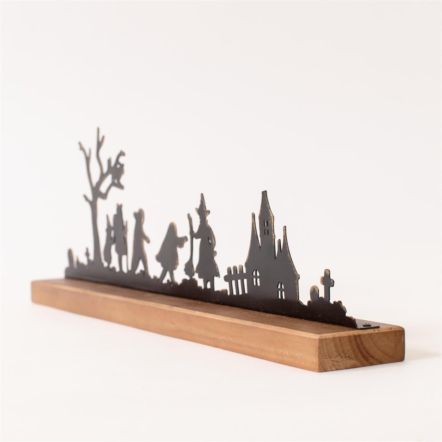 Side view of a Halloween silhouette featuring children, a witch, and haunted house made of black metal on a wooden board. 