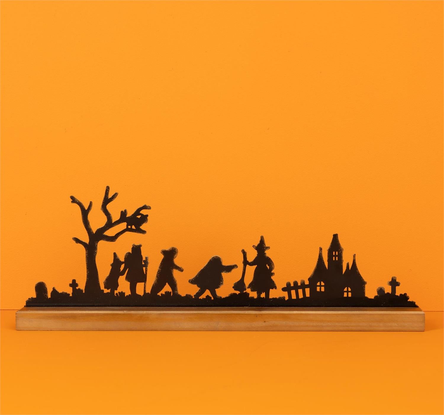 Halloween silhouette featuring children, a witch, and haunted house made of black metal on a wooden board on an orange background
