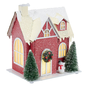 Lighted red house sitter with glittery red exterior white trim snow-dusted roof and warm glowing windows inside