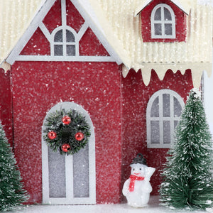 Lighted red house sitter with red glittery finish white trim green wreath red ornaments and snow-dusted roof and windows