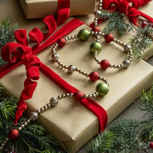 A 72 inch red bead garland made of metallic round glass beads in red green and silver draped over wrapped holiday gifts