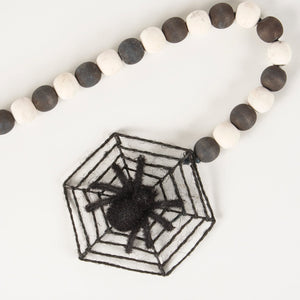 Black fuzzy spider centered in a hexagonal black yarn web on a black rings garland with alternating black and white beads