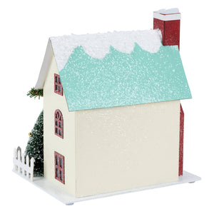 A charming lighted wreath house sitter with a glittery teal roof, cream walls, red windows, and festive greenery
