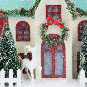 A festive lighted wreath house sitter with cream walls red windows and a sparkling green wreath above the door