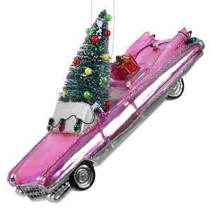A shiny pink caddy ornament made of glass with silver trim and a miniature christmas tree on the roof perfect for holiday decor