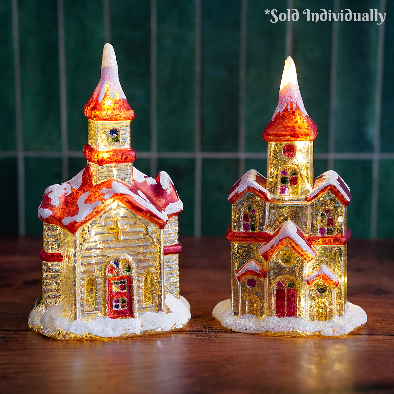 Two illuminated raz imports vintage church figurines with red gold details snow-dusted roofs lighted interiors
