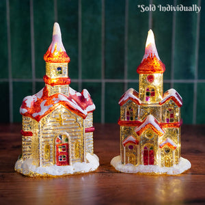 Two illuminated raz imports vintage church figurines with red gold details snow-dusted roofs lighted interiors