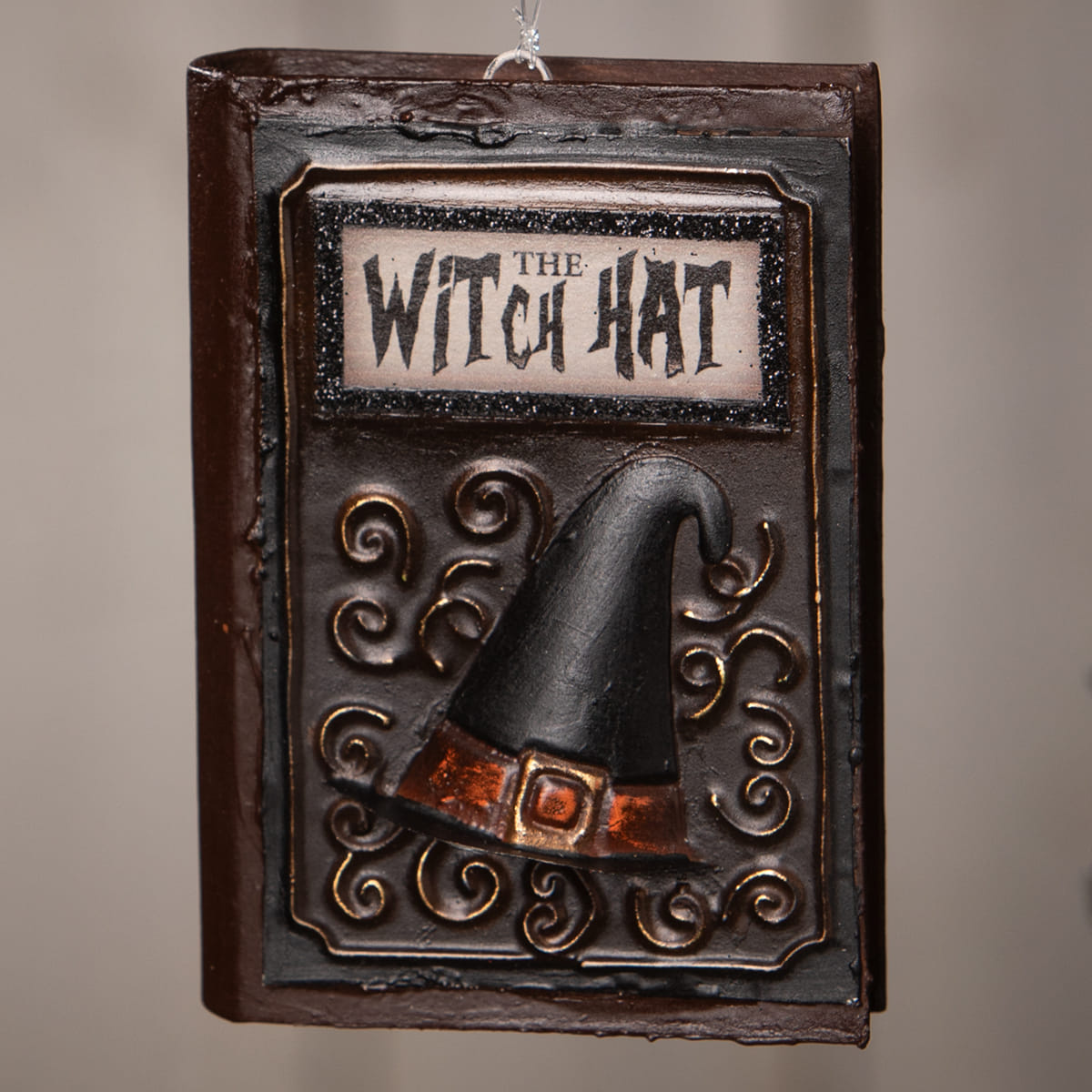 Dark brown bethany lowe witch hat book ornament with black hat, orange-brown belt, gold buckle, and ornate metal frame