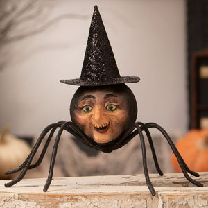 A whimsical black spider figurine with a painted human face and glittery witch hat for halloween witches decor