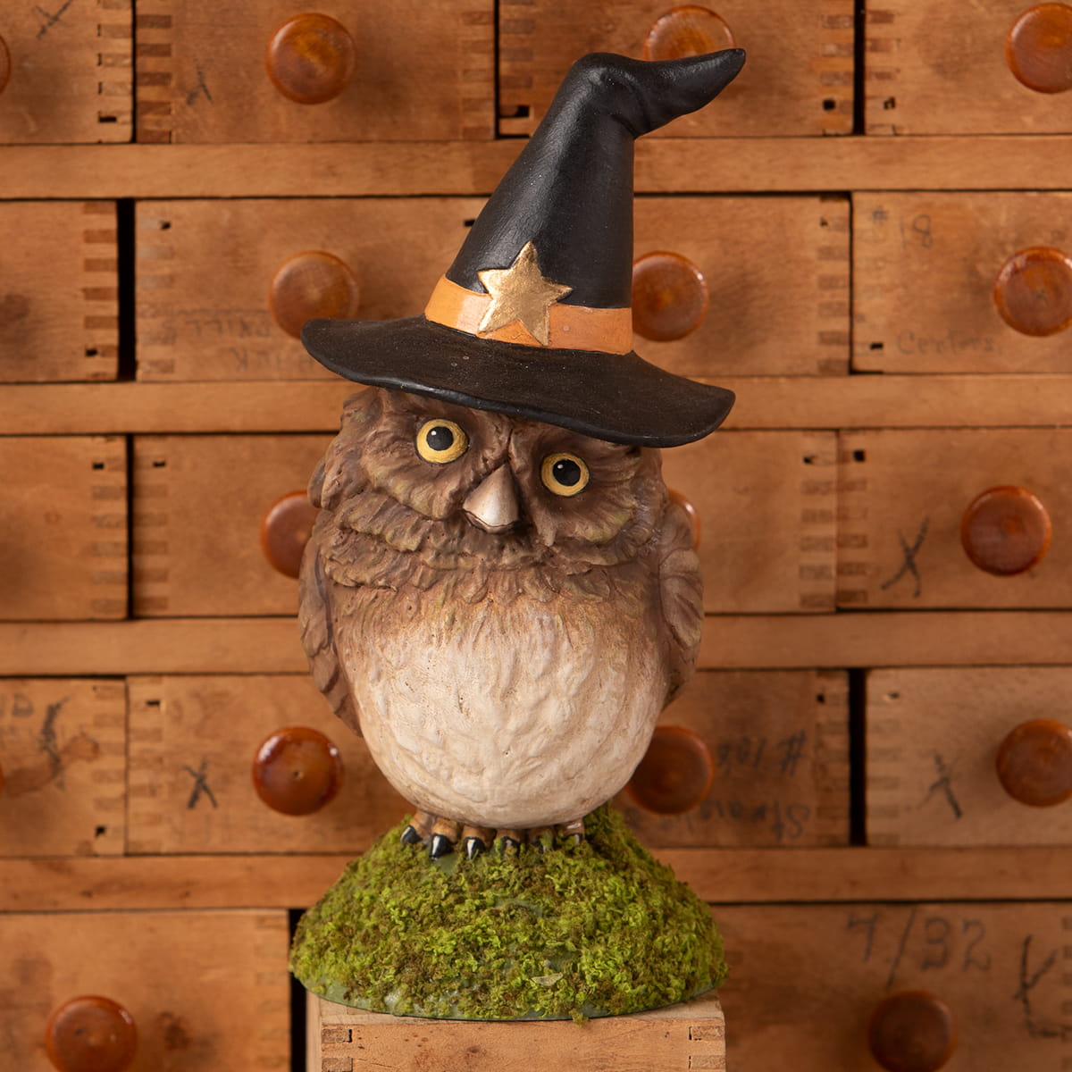 A bethany lowe design owl figurine with brown and white feathers wearing a halloween witches black hat on moss