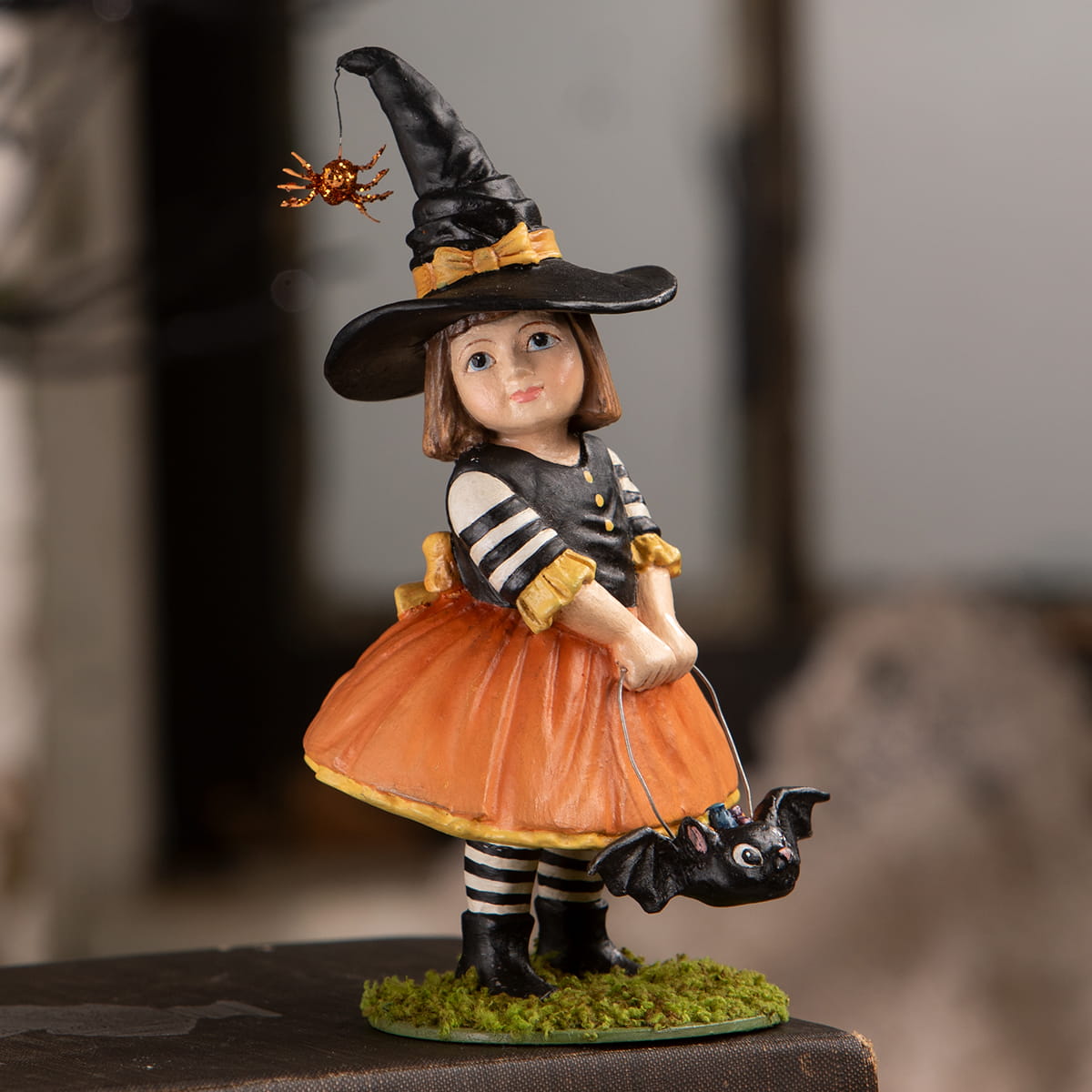 Emery witch halloween witch decor figurine in black hat with orange spider wearing striped top and orange skirt on moss