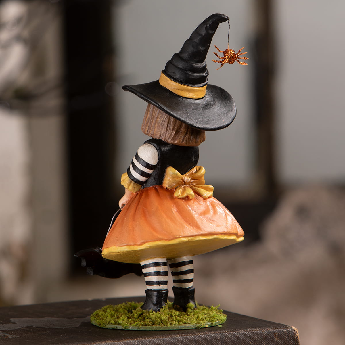 A whimsical emery witch with a black and gold hat, orange skirt, and striped leggings perfect for halloween witches decor