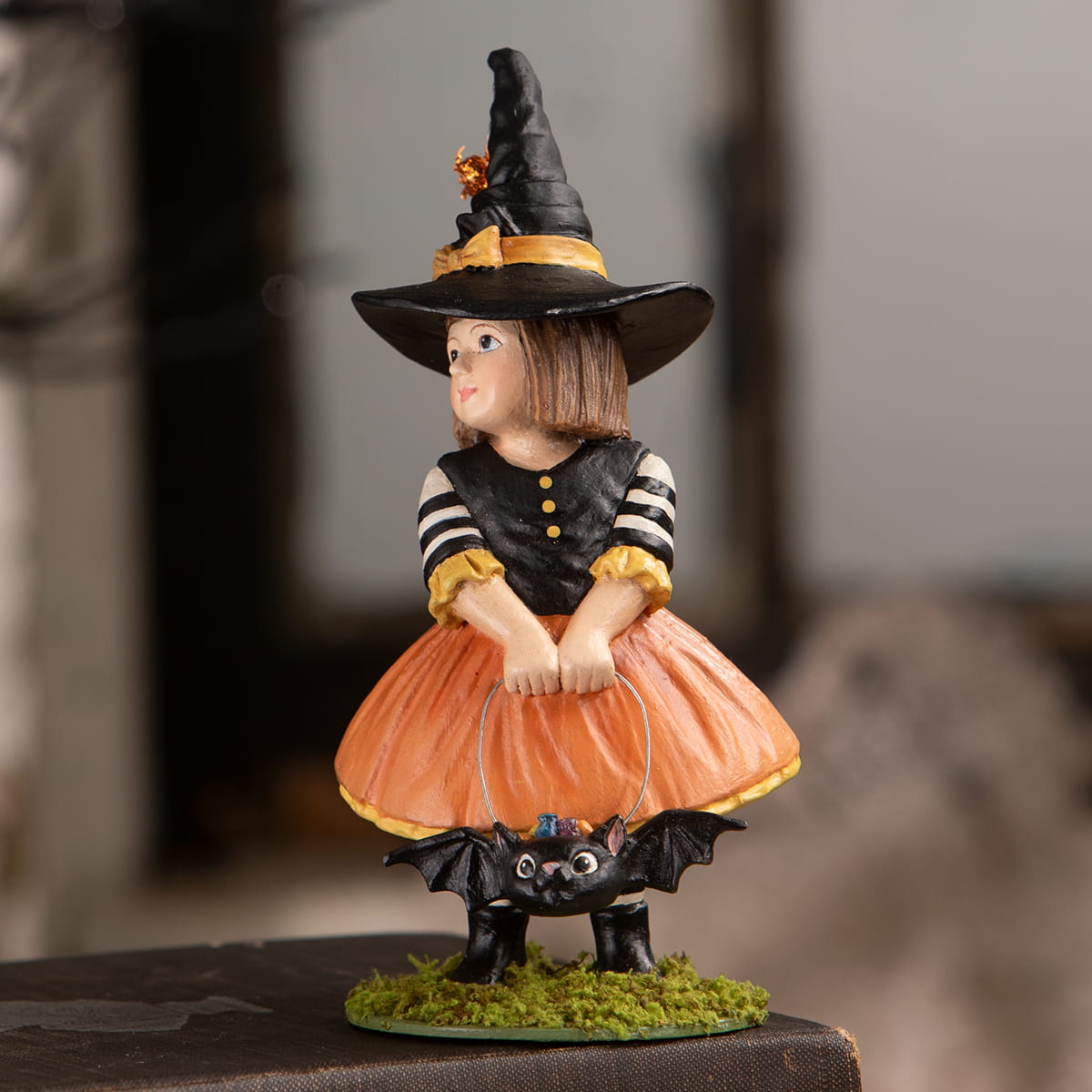 Emery witch with bat figurine with black hat and striped dress sitting on bat on moss base halloween witches decor