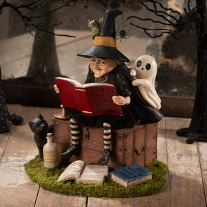 A whimsical halloween witches figurine in striped stockings reading a red book for witch decor and ghost stories