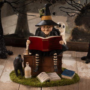 A detailed ghost stories witch figurine in black dress with striped stockings reading a red book halloween witches decor