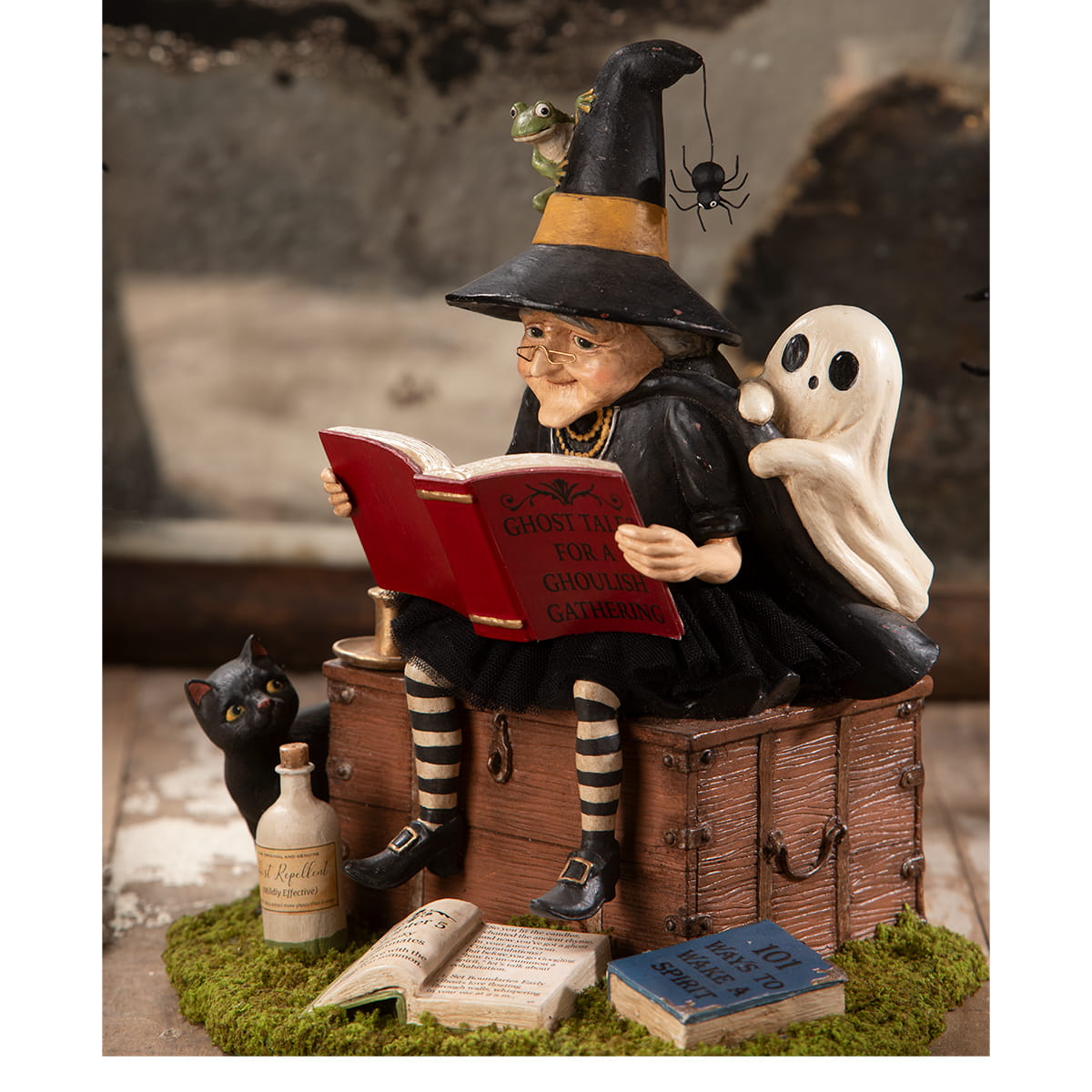 A whimsical halloween witches figurine with black and orange hat reading ghost stories atop rustic trunk decor