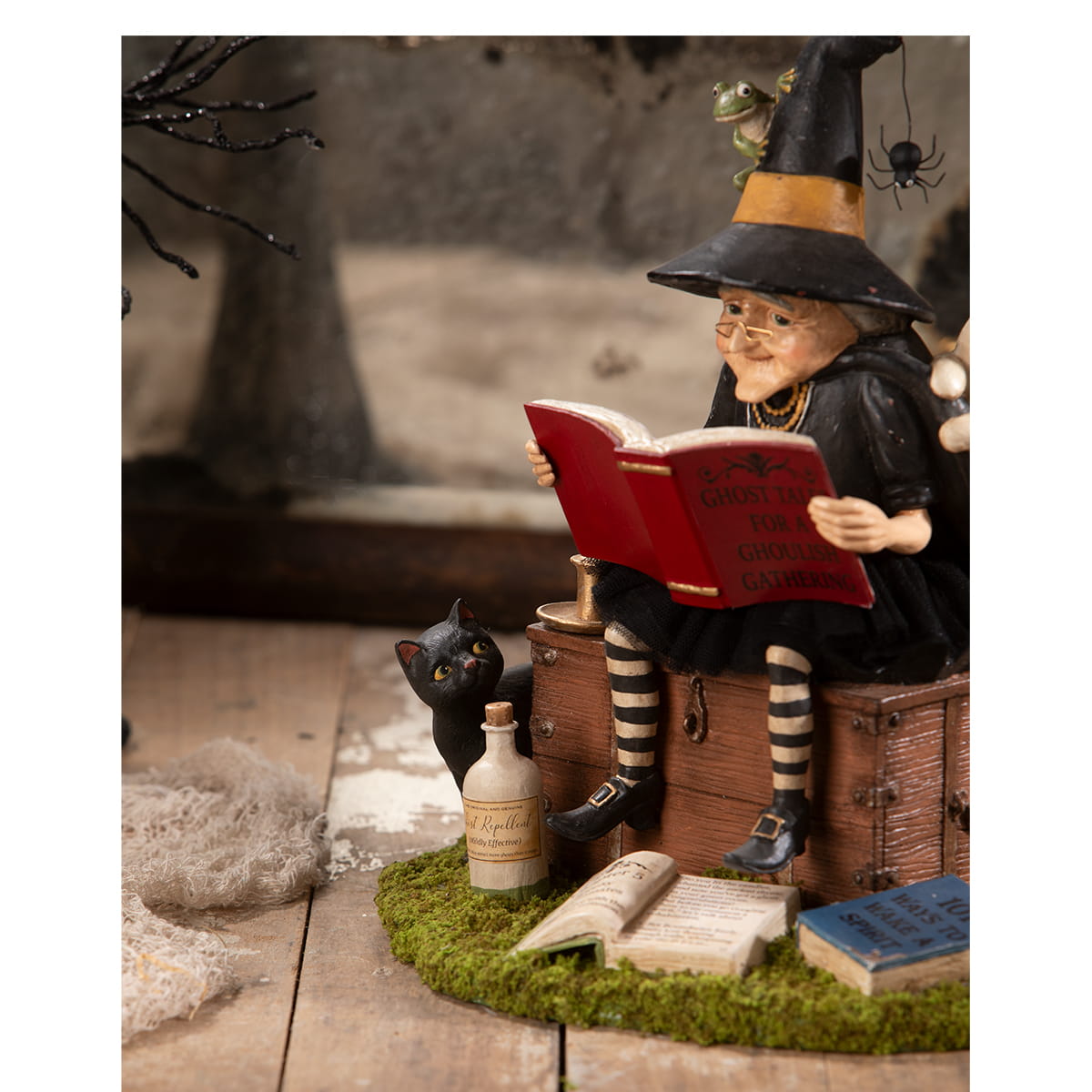 A detailed ghost stories witch figurine with glasses in black hat and cloak sitting on a chest reading a red book perfect for halloween witches and witch decor