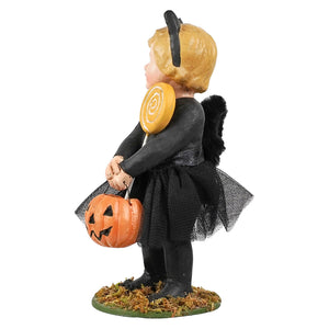 A Halloween figurine of a child dressed as a black cat, holding an orange jack-o'-lantern bucket. The figurine features blonde hair, black tail, and stands on a mossy base against a plain white background.