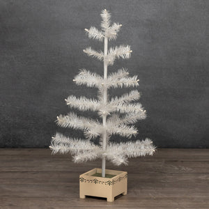 A small white feather Christmas tree with textured faux pine needles, standing in a light beige square wooden planter box on a dark wood floor against a dark gray textured wall.