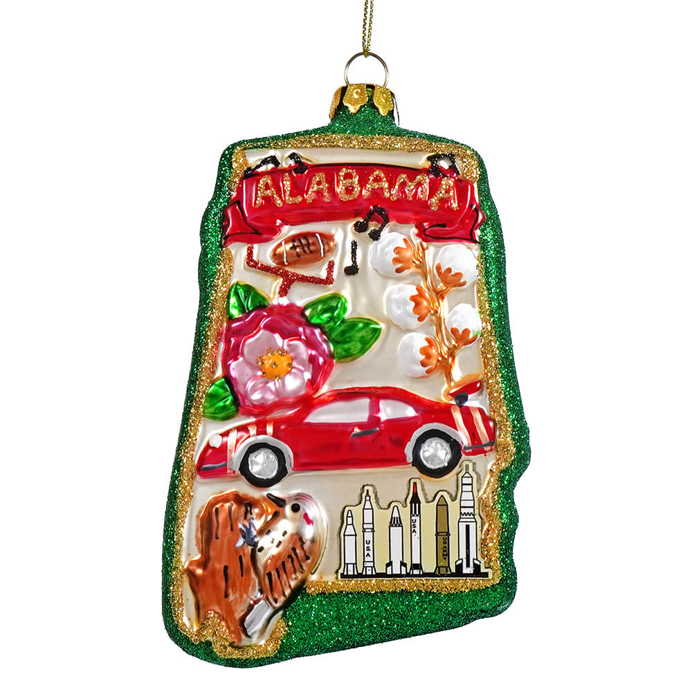 A glittery green glass alabama state ornament with red car pink flower and rocket silhouettes in ornament form