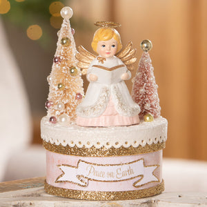 A bethany lowe angel figure with golden wings and halo on a glittery pink and gold peace on earth box