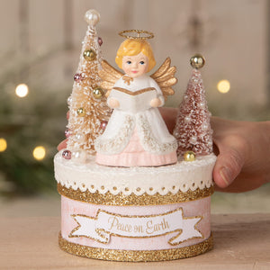 A bethany lowe pink and white angel figure with gold wings and halo holding a book on a glittery peace on earth base