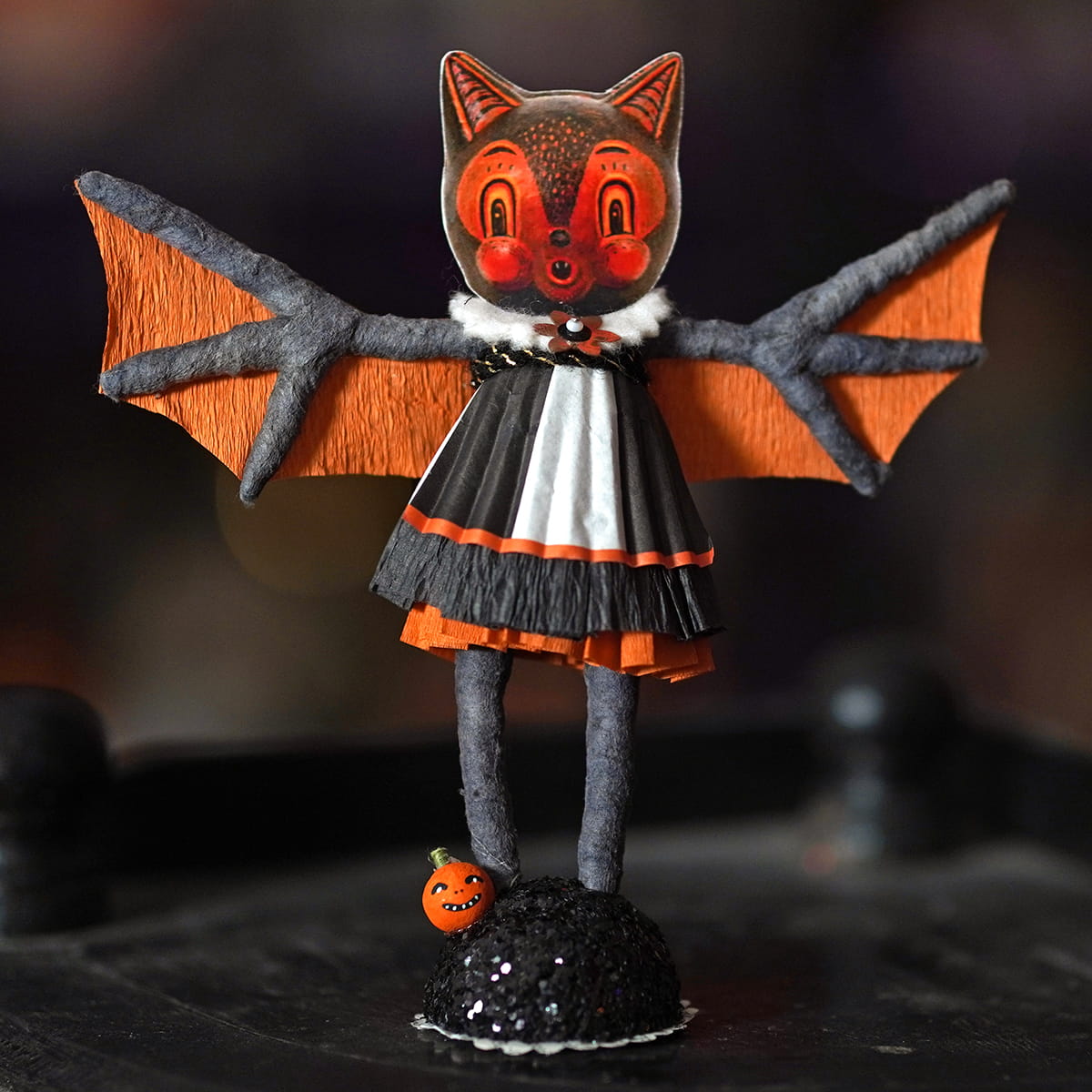 A charming bat girl figure with orange and black paper-craft bat wings, white ruffled collar, and layered dress details