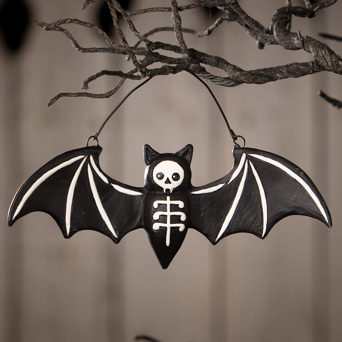 Black batty skeleton ornament with white skull face and skeletal details hanging from twisted branches by bethany lowe halloween ornaments