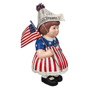 A betsy ross display figure featuring a girl in a red white striped dress holding an american flag and newspaper hat