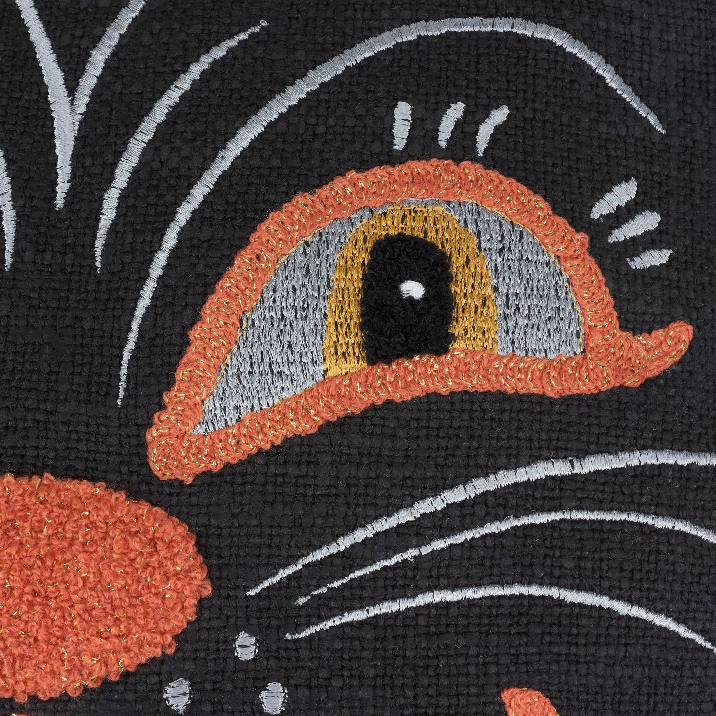 Close-up of an embroidered cat eye with orange and gray iris on a black cat face shaped pillow