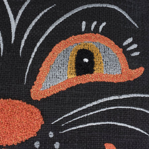 Close-up of an embroidered cat eye with orange and gray iris on a black cat face shaped pillow